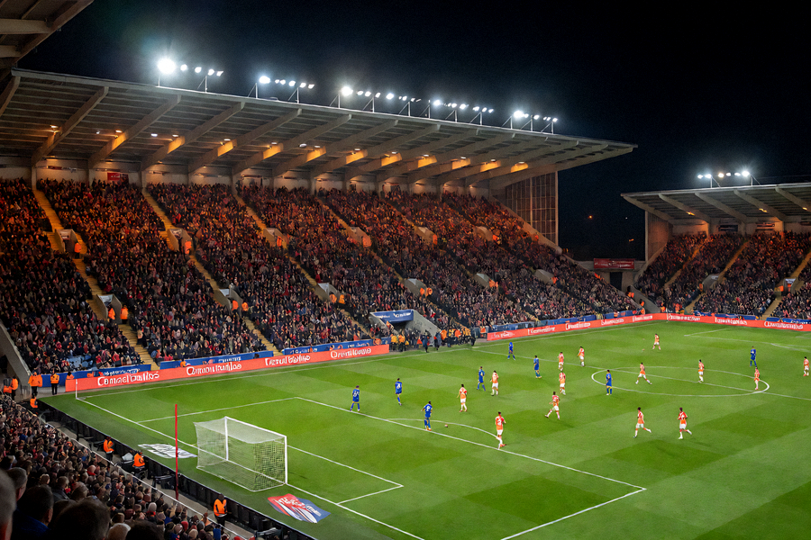 夜晚大型体育场内足球比赛正在进行，看台观众席灯火通明