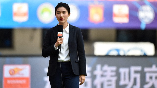 体育媒体记者在赛事新闻现场采访报道，背景为赛场标识